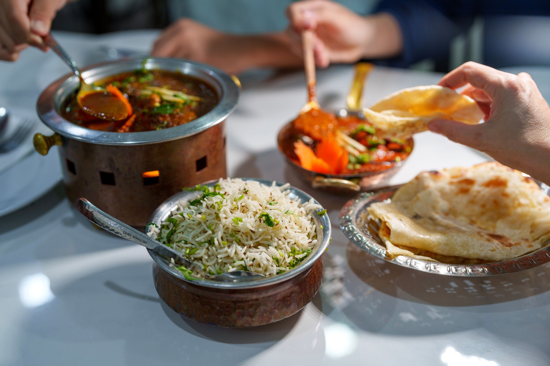 A cropped shot of people enjoying traditional Indian dish, roti naan served alongside a flavorful chicken curry and fragrant basmati rice in a restaurant.